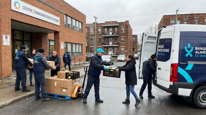 People unload food supplies from a delivery van outside a community center, organizing boxes on carts and handing them to volunteers.
